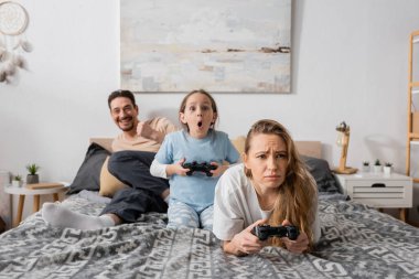 KYIV, UKRAINE - NOVEMBER 28, 2022: sad woman and shocked kid holding joysticks while playing video game 