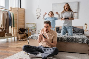 KYIV, UKRAINE - NOVEMBER 28, 2022: tensed parents playing video game near excited daughter in bedroom 