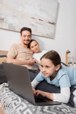 positive kid using laptop near happy parents on blurred background 