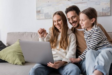 happy family smiling while looking at laptop in living room 