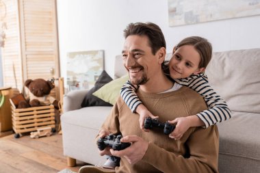 KYIV, UKRAINE - NOVEMBER 28, 2022: cheerful father and daughter holding joysticks and playing video game 