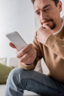 low angle view of man in beige jumper messaging on smartphone at home 