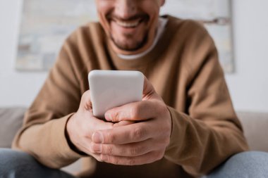 cropped view of happy man in beige jumper using smartphone at home 