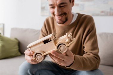 bearded man smiling while looking at wooden car toy in living room 