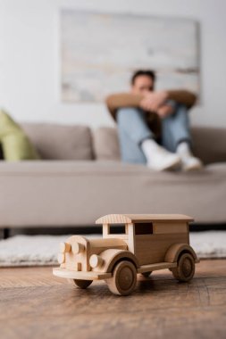 wooden car toy near blurred man sitting on couch in living room 