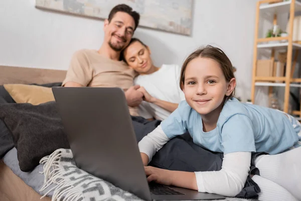 cheerful kid using laptop near happy parents on blurred background