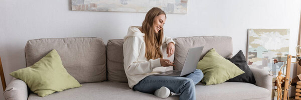 positive woman in casual clothes having video call on laptop in living room, banner 