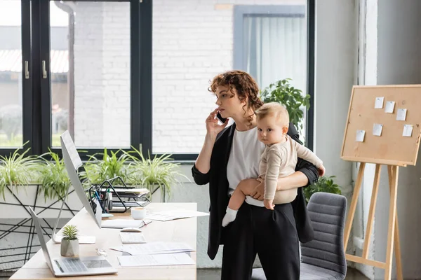 Businesswoman Talking Smartphone Looking Computer Monitor While Holding Little Daughter — Stock Fotó