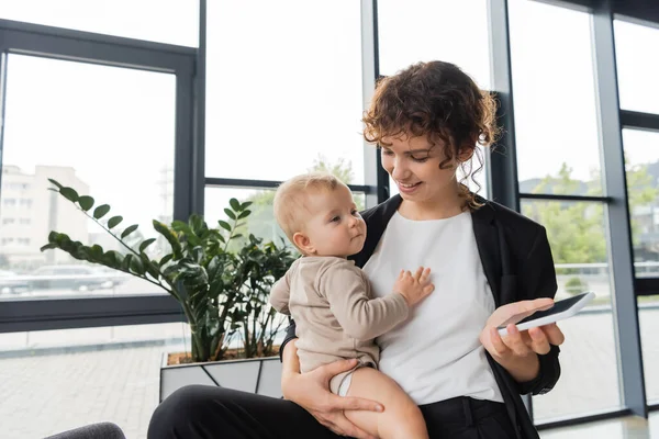 Pleased Businesswoman Holding Baby Mobile Phone Blank Screen Green Plants — Stock Fotó