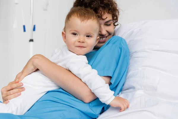 Happy Woman Patient Gown Embracing Little Daughter Bed Clinic — Fotografie, imagine de stoc