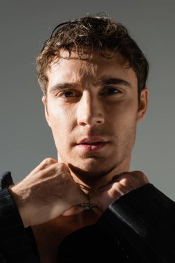 portrait of brunette man looking at camera while touching silver necklace isolated on grey