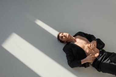 top view of sexy man with closed eyes lying in black blazer on shirtless body on grey background