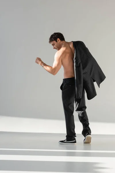stock image back view of shirtless man in black trousers and sneakers posing with blazer on grey background