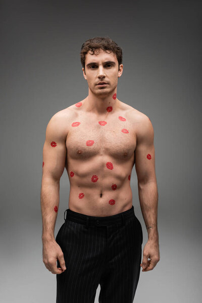 front view of sexy shirtless man with red kiss prints on body looking at camera on grey background