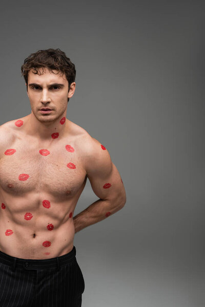 brunette man with red lipstick prints on shirtless muscular torso looking at camera on grey background