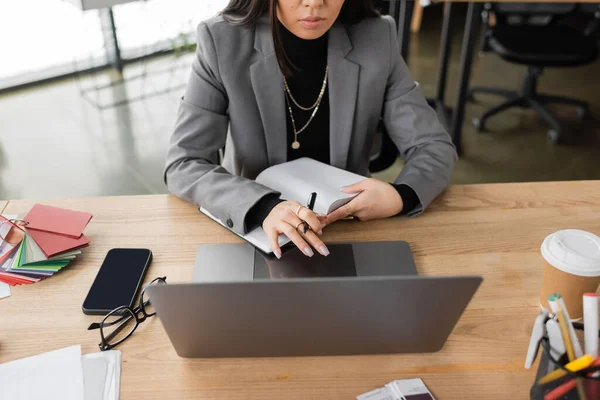 Stock image Cropped view of interior designer holding notebook near devices and color samples in office 