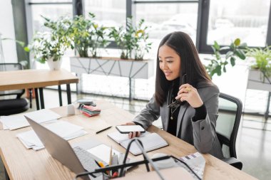 Smiling asian interior designer working with devices in office 