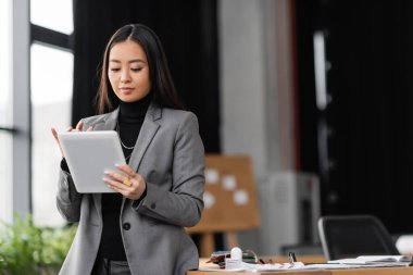 Young asian designer using digital tablet near working table in office  clipart