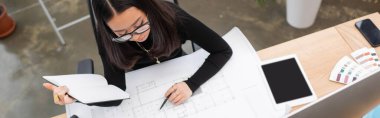 Overhead view of young asian designer working with blueprint and notebook in office, banner 