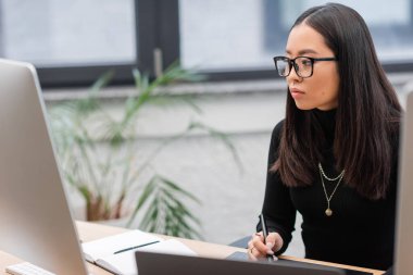 Asian interior designer using graphic tablet near computers in office 