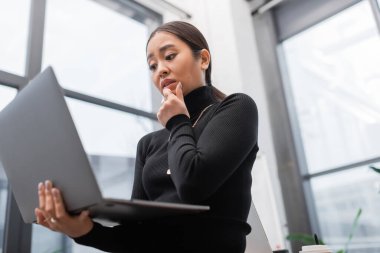 Low angle view of stressed asian interior designer looking at laptop in studio 