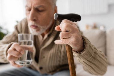 blurred man with parkinsonian syndrome holding walking cane and glass of water in trembling hands 