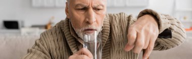 worried man with parkinsonian syndrome holding glass of water in trembling hand, banner