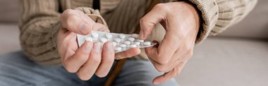 partial view of aged man with parkinson disease holding pills in trembling hands, banner
