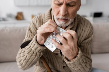 tense man suffering from parkinson disease and hands tremor holding pack of pills at home