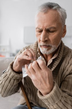 senior man suffering from parkinsonism and holding pills in trembling hands 