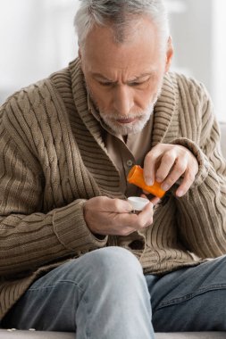 grey haired man in knitted cardigan holding pills from parkinson disease in trembling hands