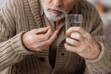 partial view of senior man with parkinson disease holding pill and glass of water in trembling hands clipart