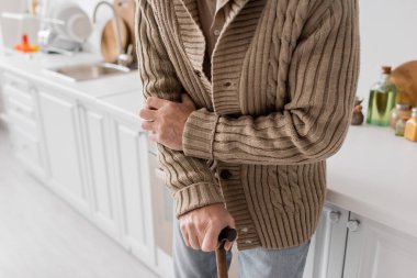 partial view of aged man with parkinson syndrome standing with walking cane in kitchen