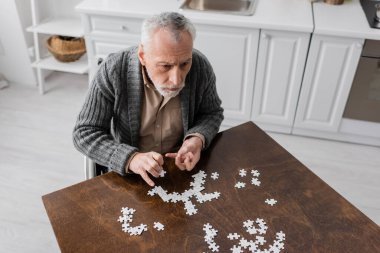 high angle view of grey haired man with parkinsonian syndrome combining jigsaw puzzle on kitchen at home