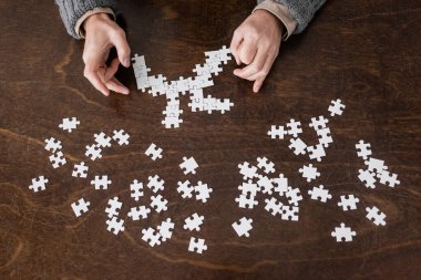 top view of cropped man with parkinson disease and hands tremor combining jigsaw puzzle on wooden table