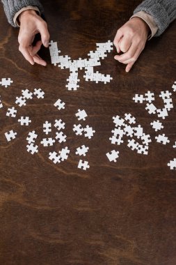 top view of cropped man with trembling hands suffering from parkinson disease and combining jigsaw puzzle on wooden table
