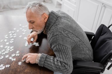 high angle view of man with parkinson disease sitting in wheelchair near elements of jigsaw puzzle