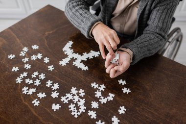 partial view of disabled man with parkinson disease holding elements of jigsaw puzzle in trembling hands