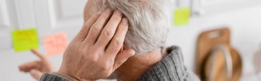 aged man with alzheimer disease touching head and pointing at blurred sticky notes in kitchen, banner clipart