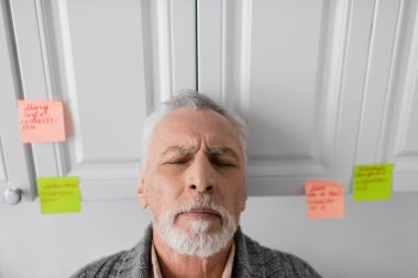 depressed man suffering from azheimers syndrome standing with closed eyes in kitchen