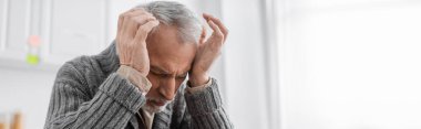 senior man suffering from azheimers disease and headache while holding hands near head, banner