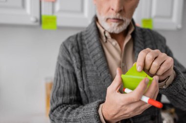 partial view of blurred senior man suffering from alzheimer syndrome and holding felt pen and sticky notes in kitchen