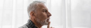 profile of senior grey haired man with alzheimer disease touching chin while thinking at home, banner