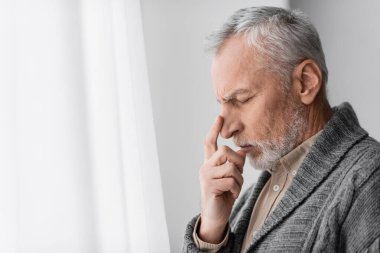 side view of depressed senior man with alzheimer syndrome touching face while standing at home