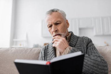 thoughtful man suffering from memory loss and looking in notebook at home