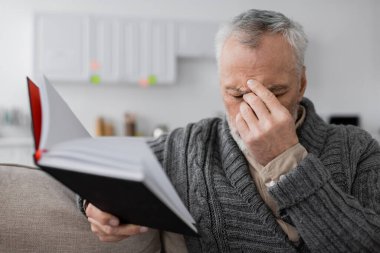 depressed man with alzheimer syndrome sitting with closed eyes and blurred notebook at home