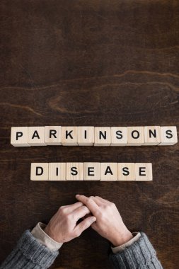 top view of cropped aged man near blocks with parkinsons disease inscription on wooden table