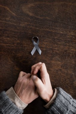 top view of cropped man with parkinson syndrome and tremor in hands near grey ribbon on wooden surface