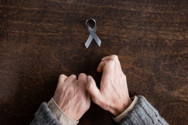 top view of cropped man with parkinsonism and trembling hands near grey ribbon on wooden table