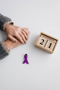 top view of purple ribbon and wooden calendar with september 21 date near cropped man with alzheimer syndrome on white surface